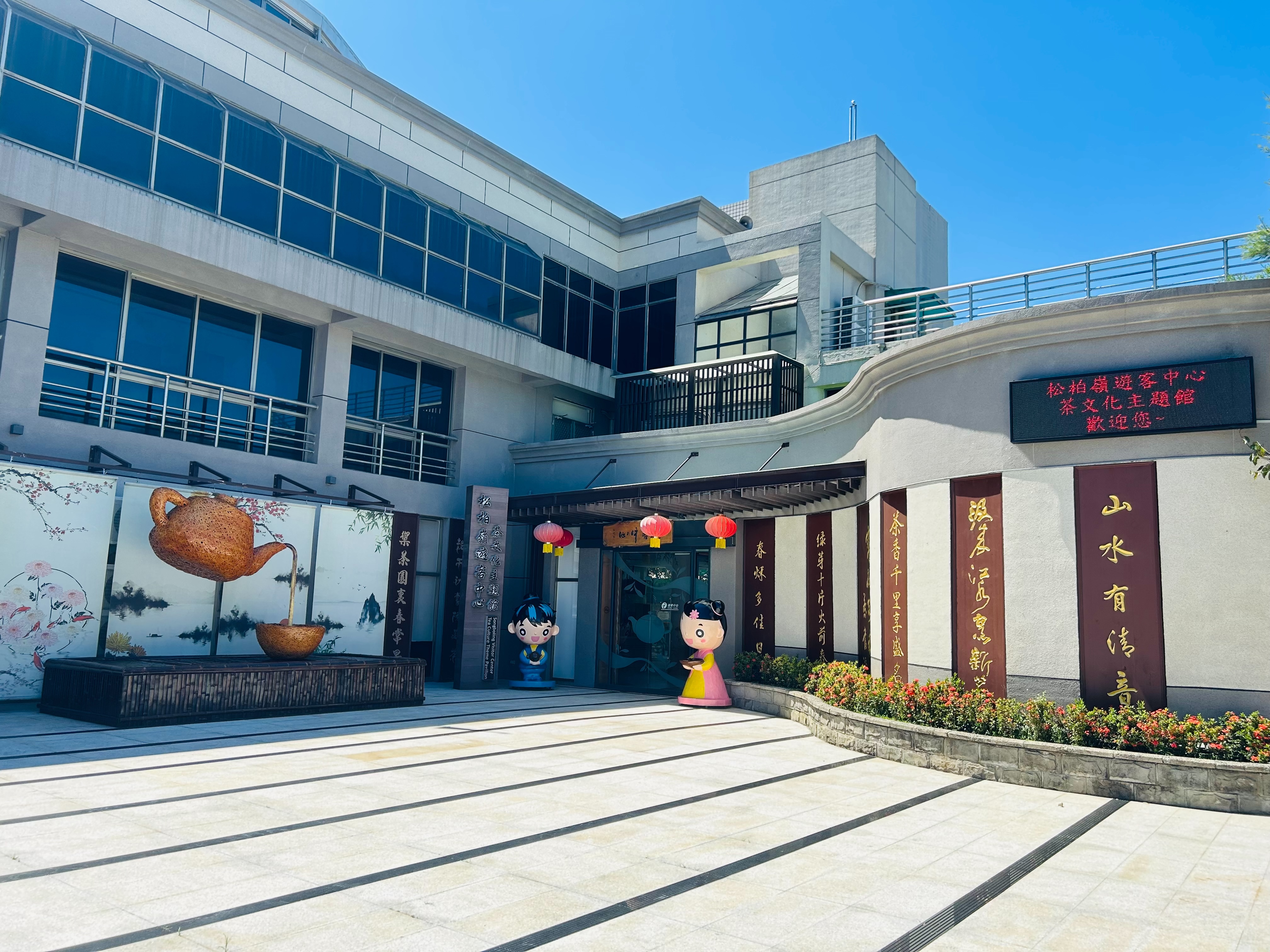 The exterior of the Songboling Visitor Center (Tea Culture Theme Building) features an ink screen with bamboo teapots to resemble a tea table, and the entrance is flanked by girls and boys serving tea, signifying that visitors are welcome.